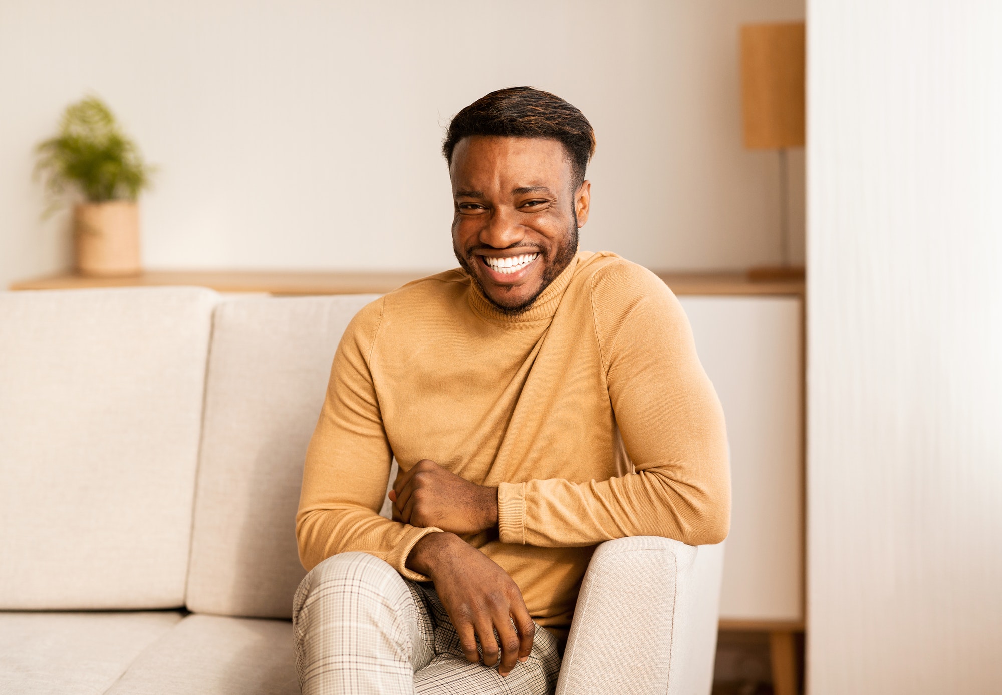 Afro Guy Smiling At Camera Sitting On Sofa At Home