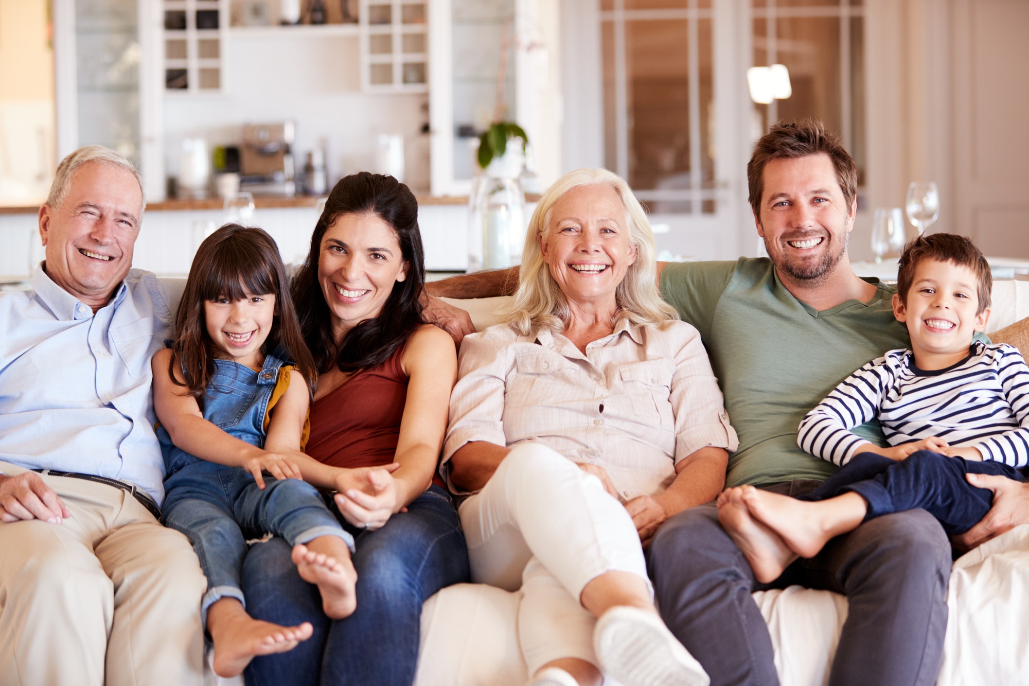 Happy three generation white family sitting on a sofa together at home smiling to camera, front view